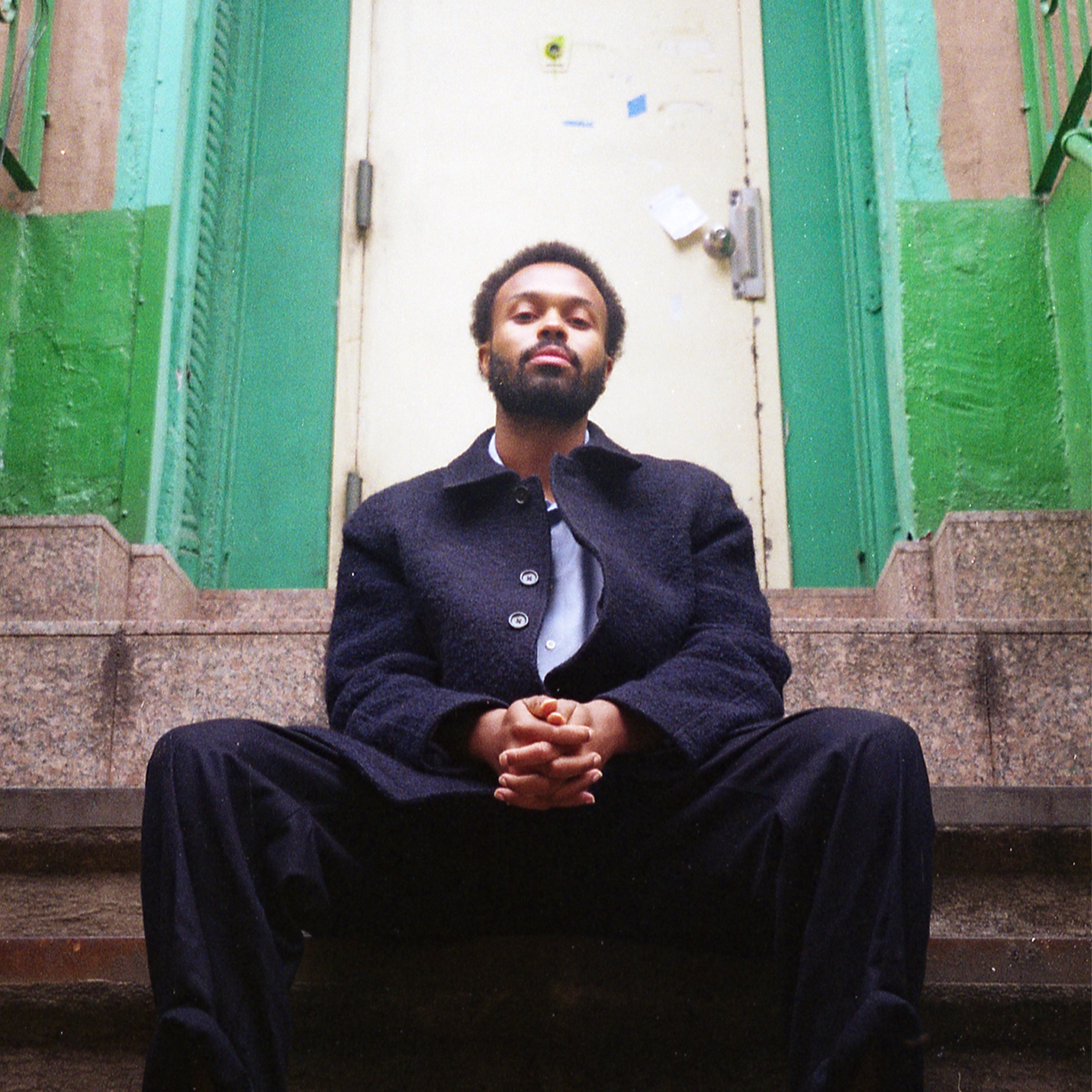 Adé Hakim seated on steps in front of a green doorway, photographed by Gabriel Gallego.