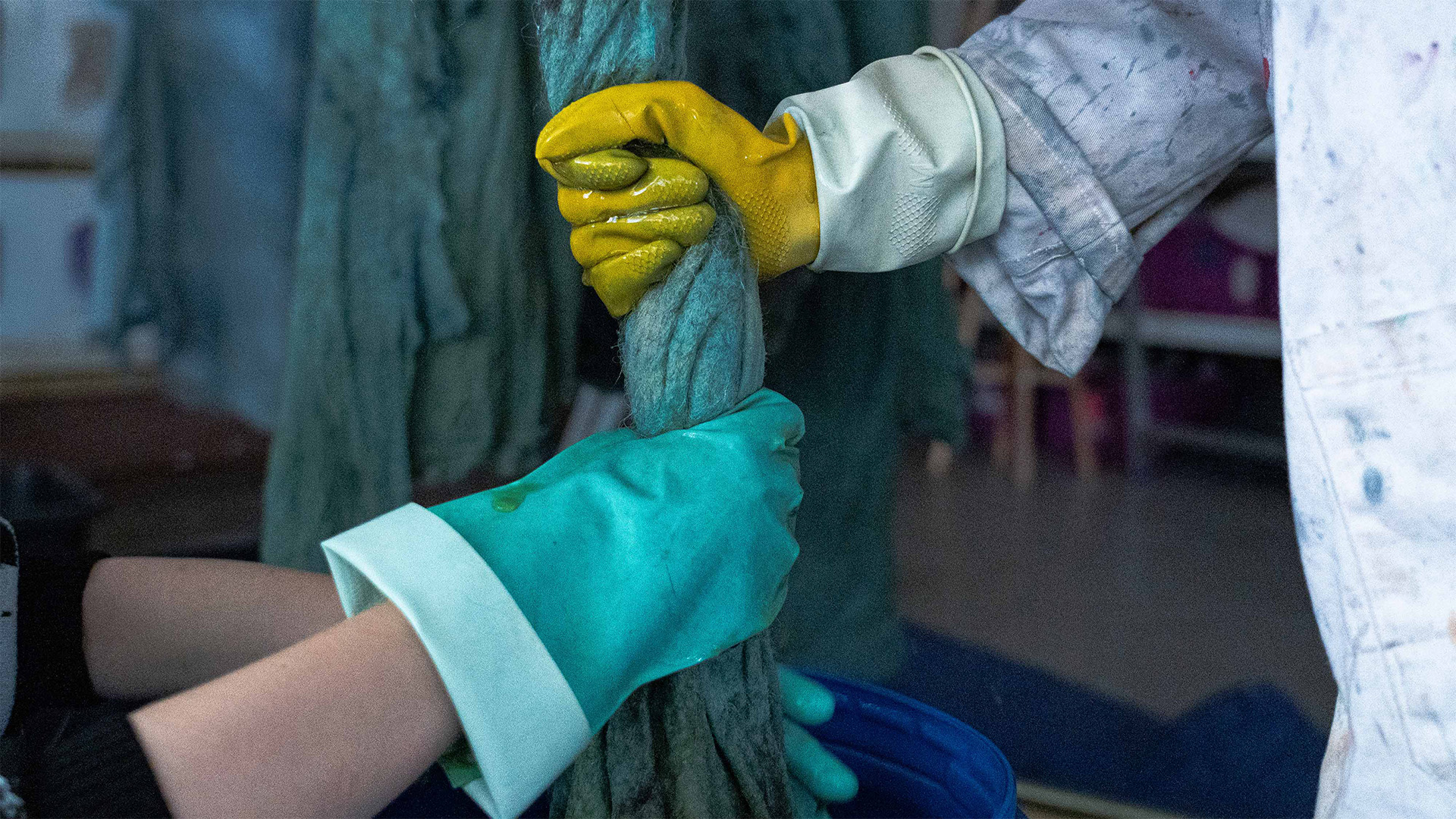 Gloved hands working with long blue-green fibres in the New Order of Fashion lab.